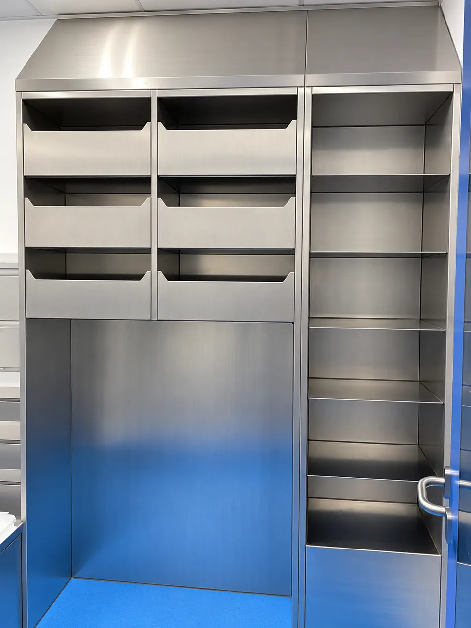Frisch gereinigte Edelstahlinstallation im blauen Raum-001-maurice-kleer metallbau saarbrücken Vestiaire en inox avec six compartiments ouverts, deux niches hautes et une colonne d’étagères latérale.